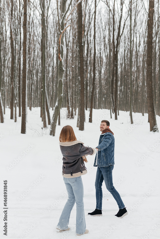 Happy couple in love on a walk in a winter park. Smiling couple holding hands walking through a snowy forest.