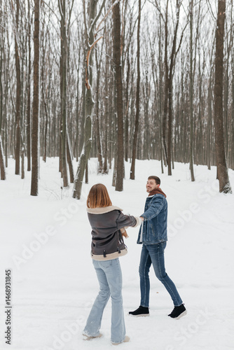 Obraz na płótnie Happy couple in love on a walk in a winter park. Smiling couple holding hands walking through a snowy forest. w salonie
