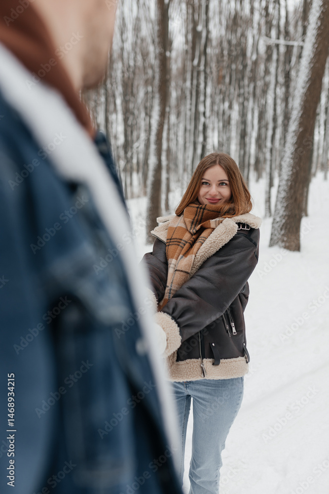 Happy couple in love on a walk in a winter park. Smiling couple holding hands walking through a snowy forest.