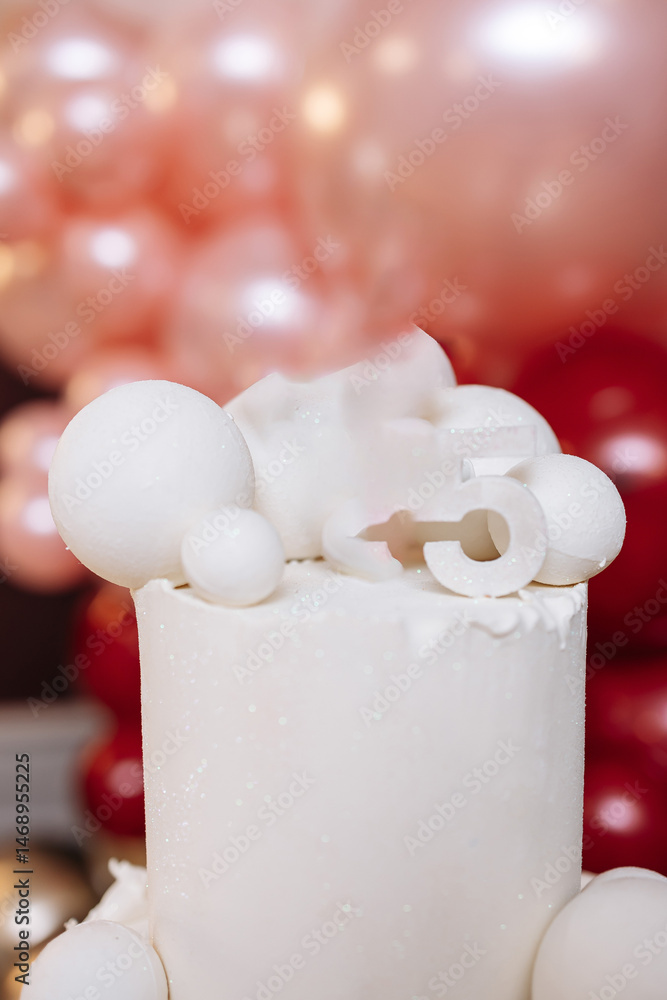 White sweet cake for birthday celebration. Large two-story cake on a background of red balloons. Festive exquisite cake for the birthday girl.