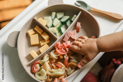 Obraz na płótnie A toddler’s chubby hands grasp colorful pasta and cheese cubes from a divided pl