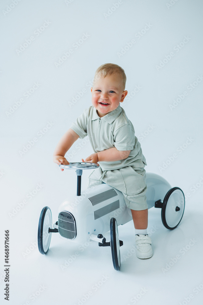 Stylish one-year-old boy in a suit with shorts and a T-shirt rides a car. Toddler boy on a white background with a toy car.