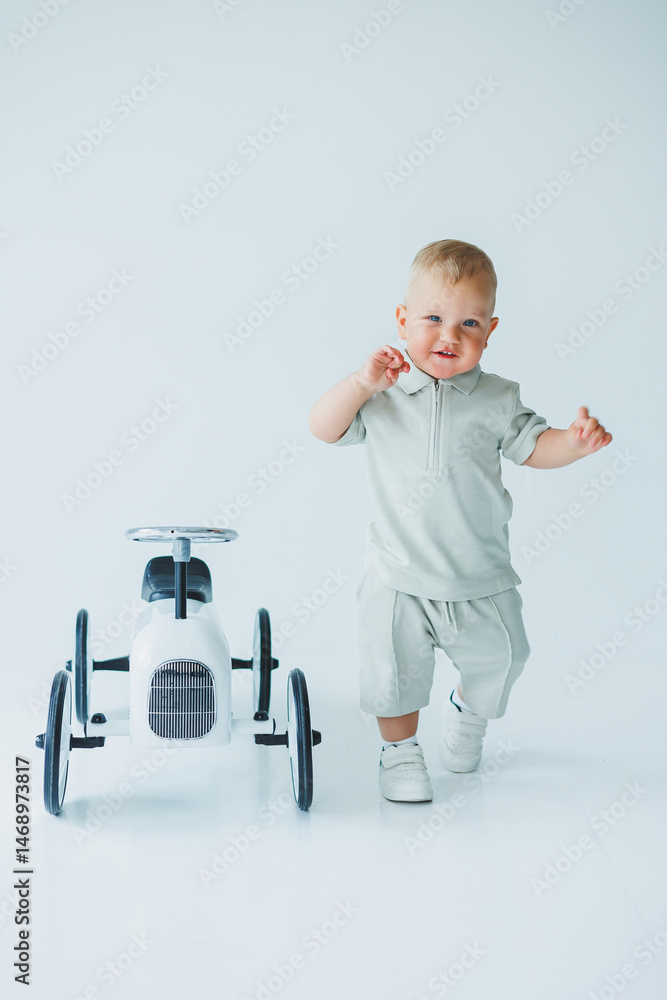 Stylish one-year-old boy in a suit with shorts and a T-shirt rides a car. Toddler boy on a white background with a toy car.