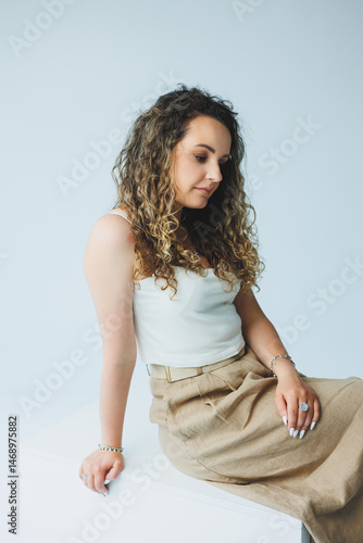 Obraz na płótnie Curly pretty woman sitting in the living room on the sofa and smiling dreamily. Woman in a white top and skirt with a romantic mood sitting in the living room. w salonie