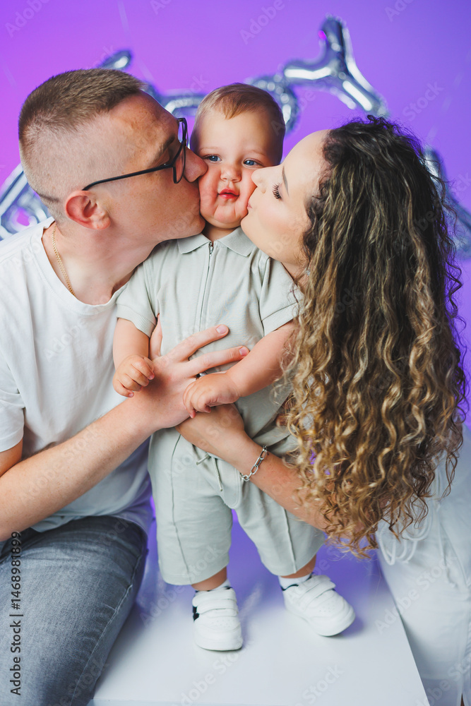 Young mom and dad on a white background playing with their one-year-old son. Toddler boy and mom and dad laughing hugging. Happy mom dad with child.