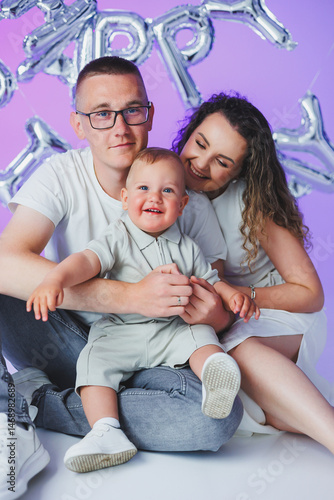 Obraz na płótnie Young mom and dad on a white background playing with their one-year-old son. Toddler boy and mom and dad laughing hugging. Happy mom dad with child. w salonie