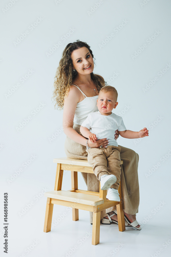 Young mother on a white background playing with her one-year-old son. Toddler boy and mother laughing hugging. Happy mother with child.