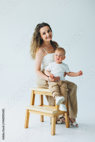 Obraz na płótnie Young mother on a white background playing with her one-year-old son. Toddler boy and mother laughing hugging. Happy mother with child. w salonie