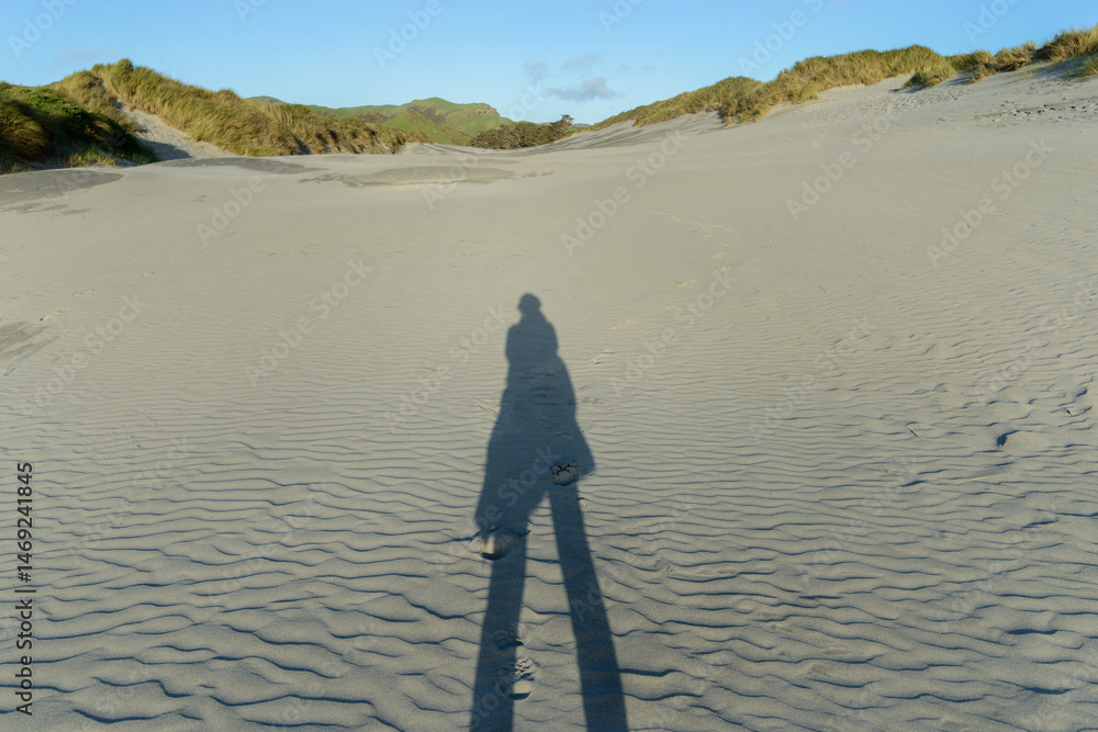 Long shadow of a woman on sand dunes. Wharariki Beach. Golden Bay. South Island.