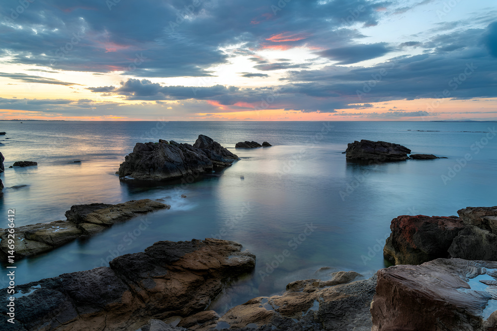 Fototapeta premium Rocky formations in calm ocean at vibrant sunset