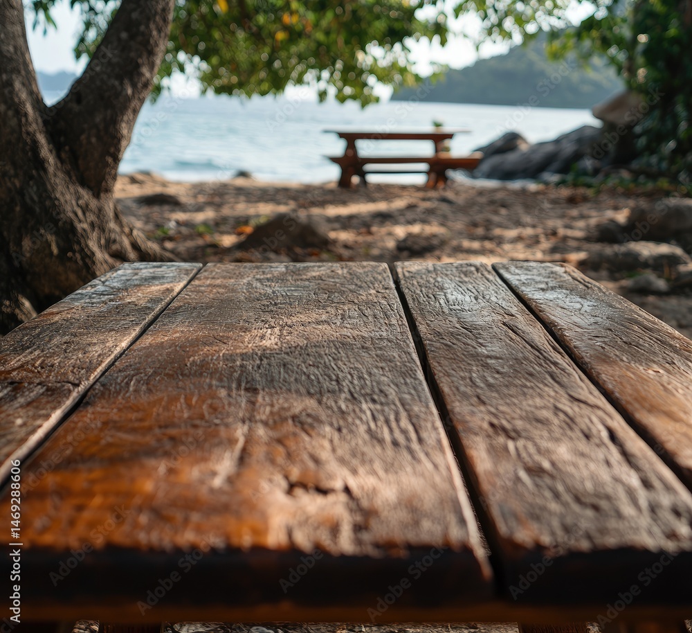 Fototapeta premium Close-up of a weathered wooden table on a sandy beach, with a blurry picnic table in the background