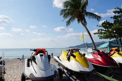 Φωτογραφία Jet skis lined up on a sandy beach with palm trees and calm ocean under bright s