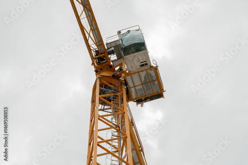 A tall crane on a construction site, blue sky. Construction crane in the sky. Yellow crane tower lifting up