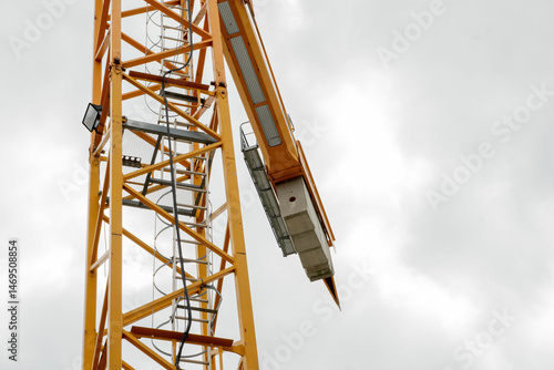 A tall crane on a construction site, blue sky. Construction crane in the sky. Yellow crane tower lifting up