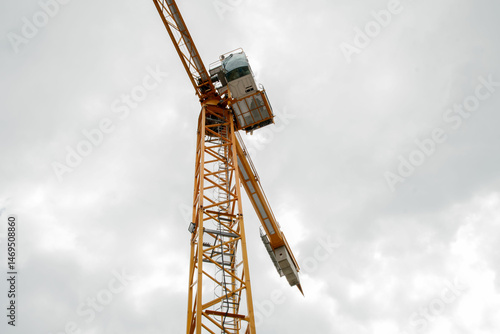 A tall crane on a construction site, blue sky. Construction crane in the sky. Yellow crane tower lifting up