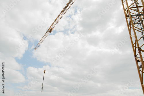 A tall crane on a construction site, blue sky. Construction crane in the sky. Yellow crane tower lifting up