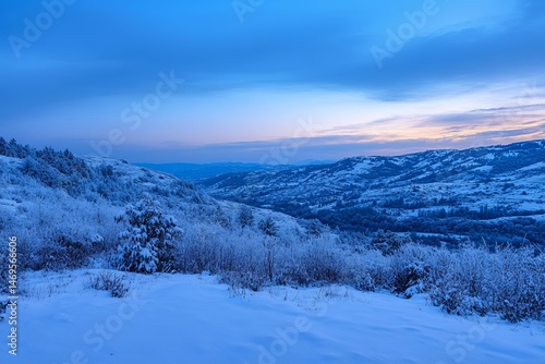Snowy mountain peaks glowing in sunrise light above a quiet winter valley in blue hour