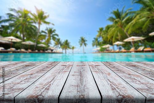 Beautiful tropical resort poolside with wooden deck and palm trees under clear blue sky