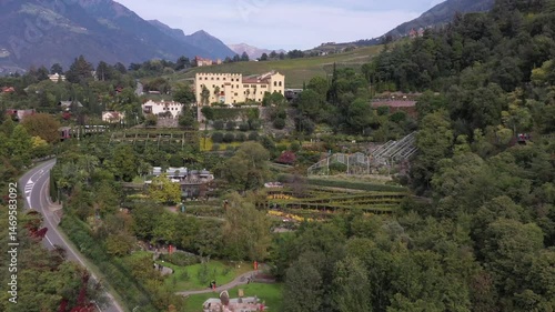 Panorama mit Schloss inmitten von Gärten und umgeben von grünen Bergen, ein idyllisches Naturszenario, Video, Drohne, Drohnenaufnahme, Gärten von Schloss Trauttmansdorff, Meran, Trentino, Südtirol