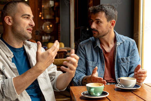 Cuadro en lienzo Two men sitting together at a table in a cafe, enjoying coffee and engaging in a