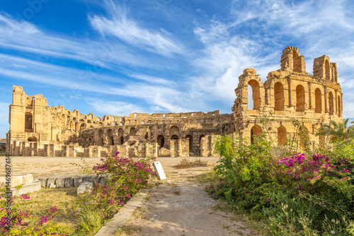 Entrance to ancient african Roman Colosseum amphitheatre arena panorama with ruins and columns and flowers in the foreground, El Jem, Mahdia, Tunis