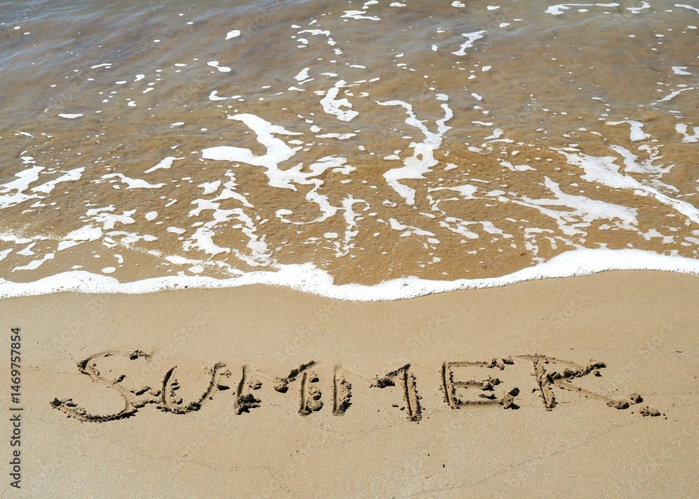 Fototapeta premium Palabra verano (summer) escrita en la arena de la playa con ola espumosa
