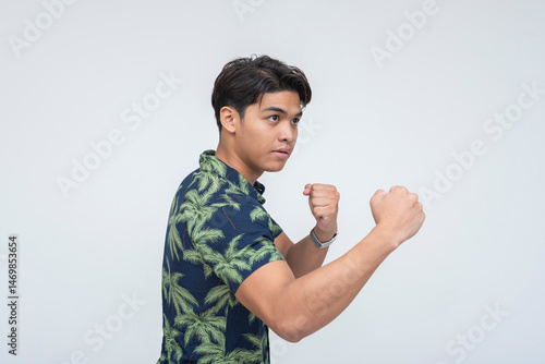 Fotografi Side view of a serious Southeast Asian man in fighting stance with fists up, suggesting a heated physical confrontation or self-defense
