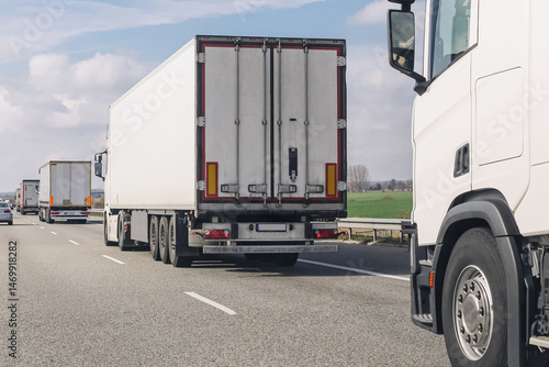 Cargo trucks driving on highway. Logistic transport on asphalt road. Freight vehicles in traffic. Delivery service and commercial shipping. Modern transportation scene in daylight.