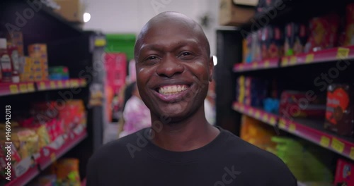 Wallpaper Mural African descent man smiling in grocery store aisle, close to camera, surrounded by colorful product shelves, wearing black t-shirt and looking directly at camera Torontodigital.ca