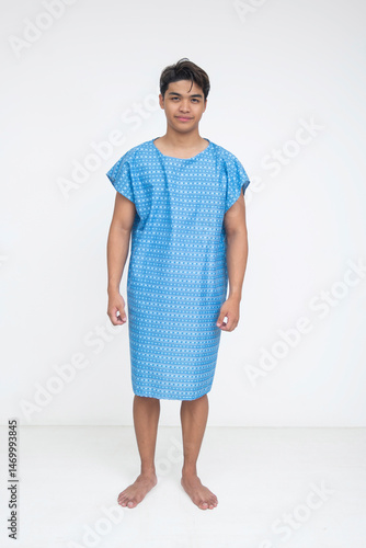 Full-length image of a young Southeast Asian male in a hospital gown, standing barefoot and facing forward. Isolated on a light background.