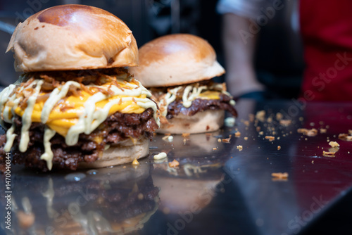 Freshly made double smash burgers with melted cheddar, grilled onions, and sauce on a shiny countertop..