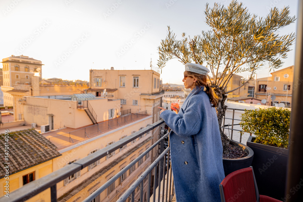 Fototapeta premium Stylish woman with drink enjoys golden hour on a rooftop terrace in Rome. Scenic view over domes, monuments, and ancient ruins