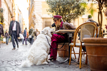 A stylish woman enjoys coffee at an outdoor cafe in Rome while bonding with her large white dog. The image conveys European lifestyle travel and emotional pet connection
