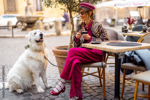 Photography A fashionable woman in vibrant clothes sits at an outdoor cafe in Rome with her white dog