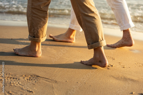Close-up of couple's bare feet walking on sandy beach at sunset. Lifestyle. Vacations.
