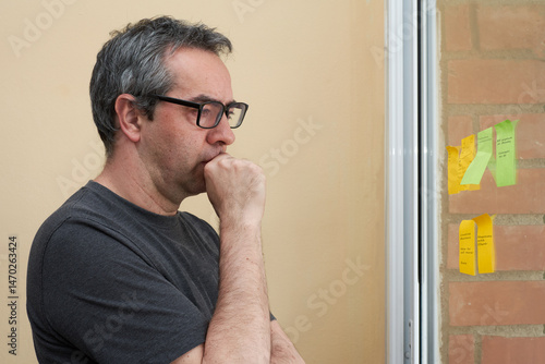 Stressed man looking at sticky notes while feeling overwhelmed. Concept of mental overload, work pressure, decision fatigue, and stress management.