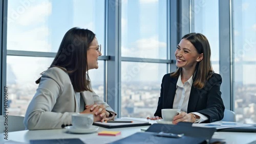 two businesswomen talking while sitting at a table in an office