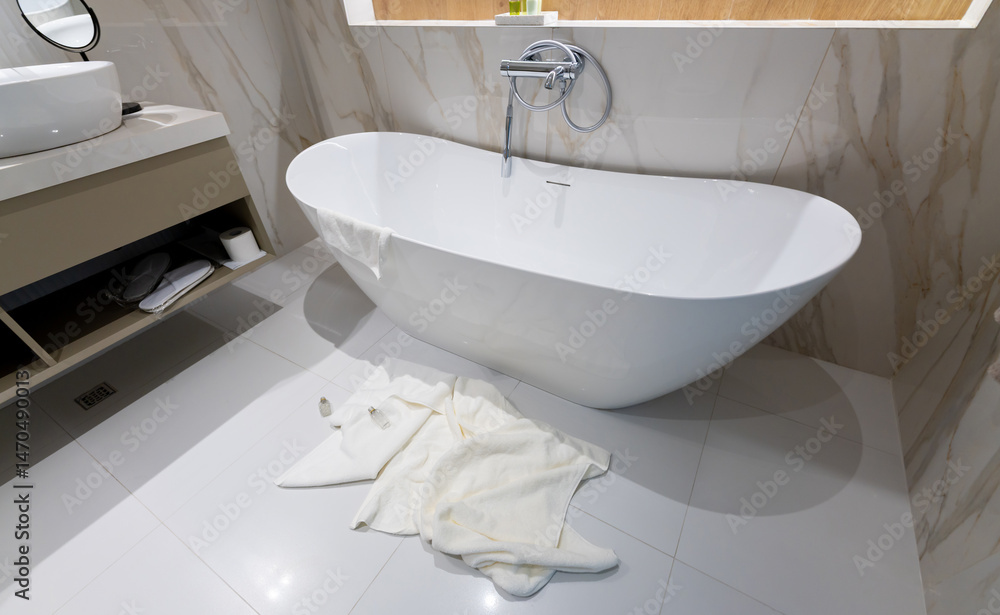 Fototapeta premium A modern freestanding bathtub in a luxury bathroom with towels left on the floor