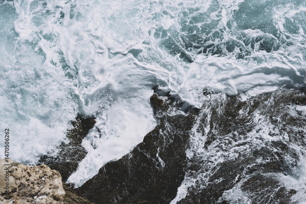 Obraz premium Dynamic ocean waves crashing over rugged coastal rocks with white foam