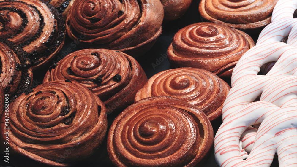 Fototapeta premium A variety of pastries, including cinnamon rolls and a donut with a white stripe, are displayed on a counter. cinnamon rolls are brown and have a spiral shape, while the donut is white.