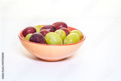 Close-up of fresh grapes in a small bowl, on a white background.