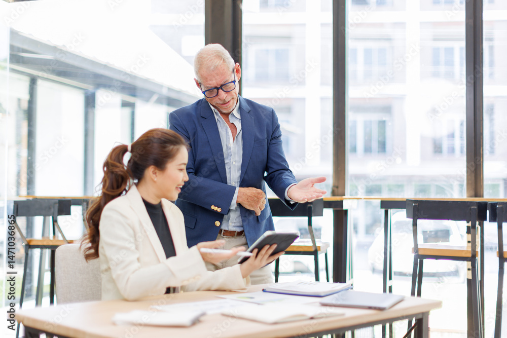 Obraz premium Two business people, a business man and a business woman, engage in a discussion as they read a financial report together. asian business professionals working together in a modern finance company.