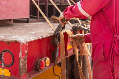 фотографія Action of a worker is tightening latching strap belt to secure the load object on trailer truck