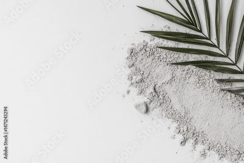 Light gray powder with palm leaf.  A scattering of light gray powder forms a loose pile on a white background, with a single, vibrant green palm leaf positioned at the upper right
