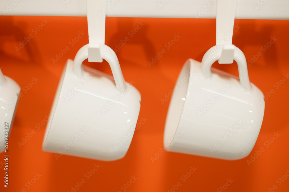 Obraz premium White ceramic mugs hanging on a bright orange wall in a cafe