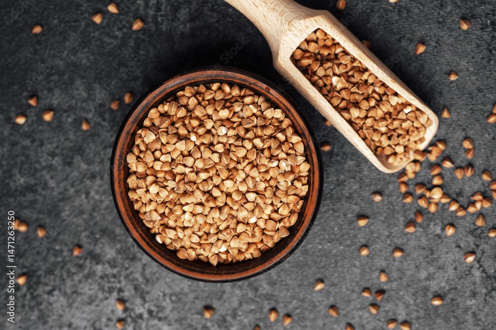 Buckwheat grains in a bowl with a scoop on a dark textured surface Buckwheat grains in a bowl with a scoop on a dark textured surface