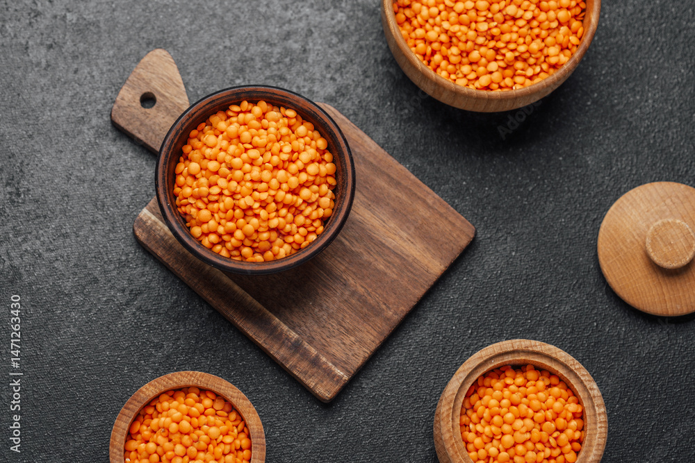 Bright orange lentils arranged in wooden bowls on a dark surface
