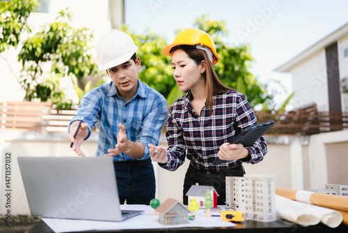 Wallpaper Mural Two engineers wearing hard hats discuss blueprints and plans at an outdoor construction site, using laptops to review architecture. Torontodigital.ca