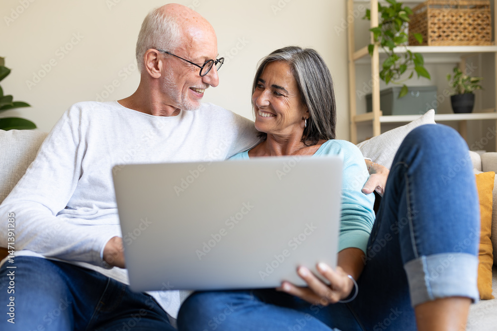 Happy mature married couple in love using laptop relaxing on the couch at home living room looking at each other. Happy mature married couple in love using laptop relaxing on the couch at home living room looking at each other.