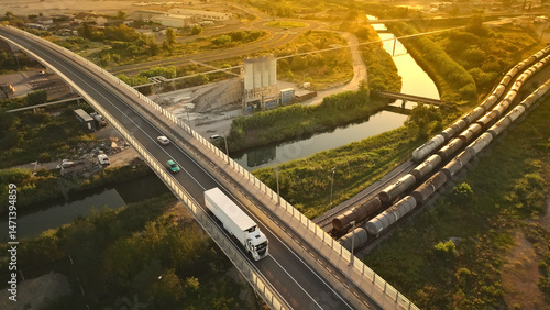 Aerial view of a busy highway with a truck and cars, a train track, and a river, illustrating the interconnectedness of transportation and cargo distribution.
